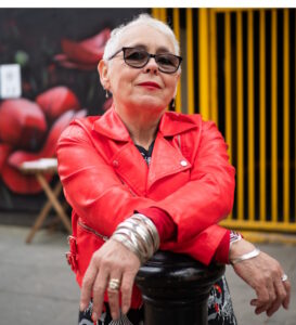 Hip looking senior women, short white hair, red leather jacket, bulky jewelry and sunglasses with cheeky smile