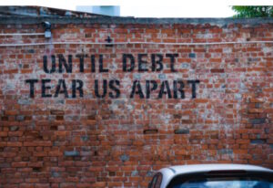 Brick wall with the following written on it: "Until debt tear us apart."