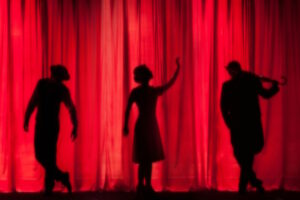 silhouette of three performers on stage in front of red curtain
